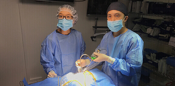 Medical team in surgical attire performing a procedure under bright operating lights in a clinical setting.